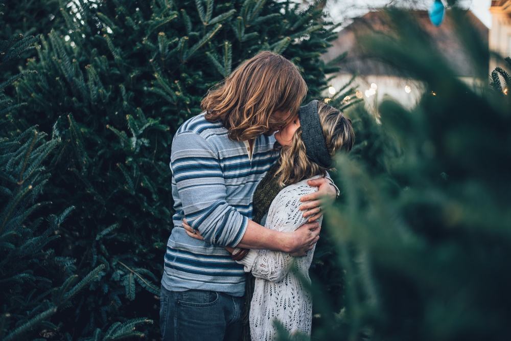 Hippie Couple Kissing Between Christmas Trees