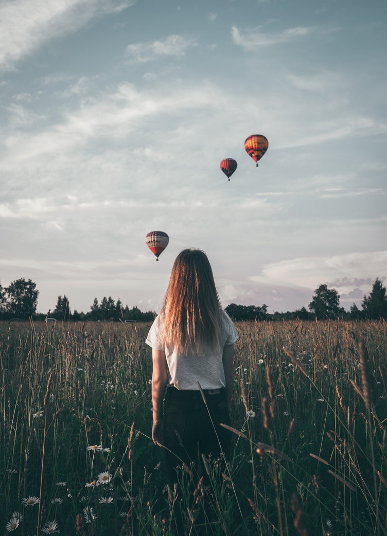 young girl walking in a meadow fields with hot air balloons floating by her