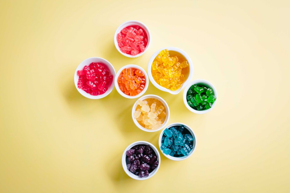 Colorful gummy bears neatly placed inside small white bowls on a yellow table