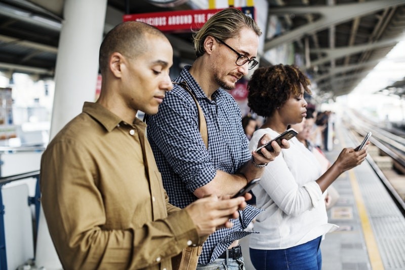 three people waiting for the metro using their cellphones