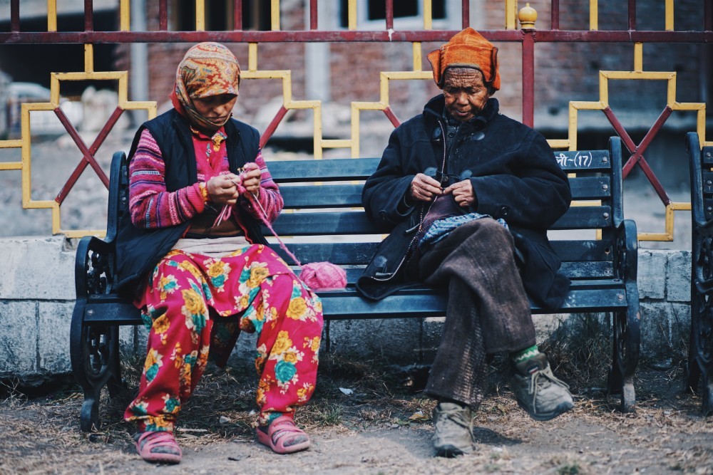 Two Older Women Sitting on a Bench and Weaving