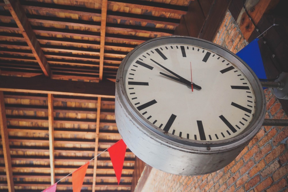 Classic black and white clock attached on a wall in front of paper celebration flags.