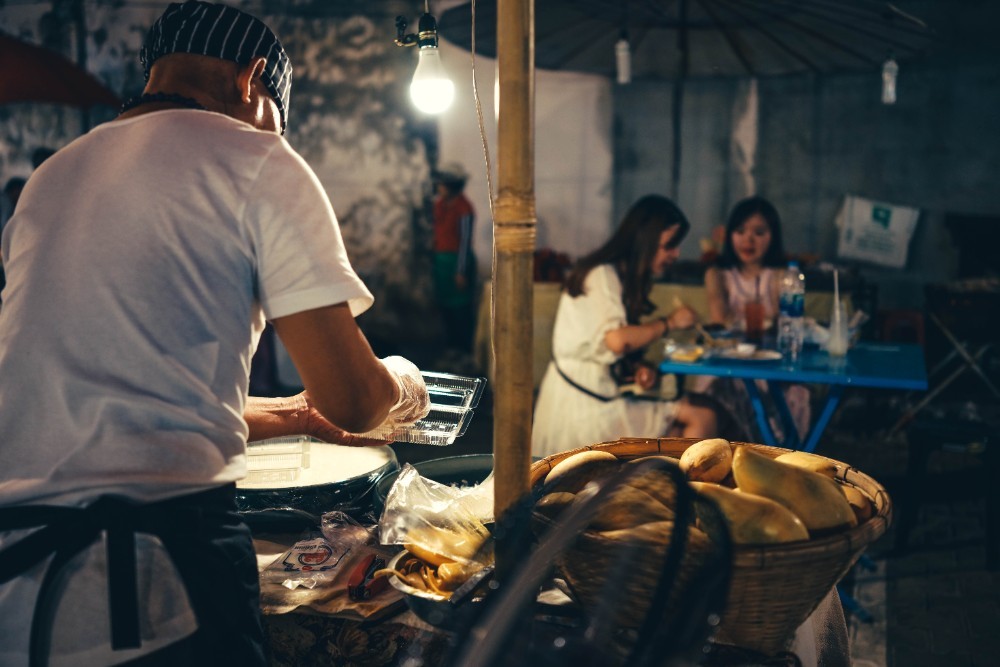 Man working behind a fruit stand at the night market photographed from behind.