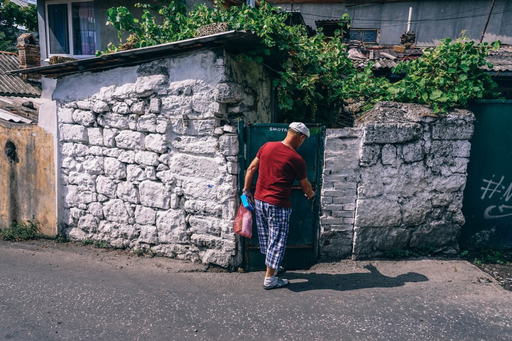 Man Unlocking his Gate while Holding a Plastic Bag with Groceries