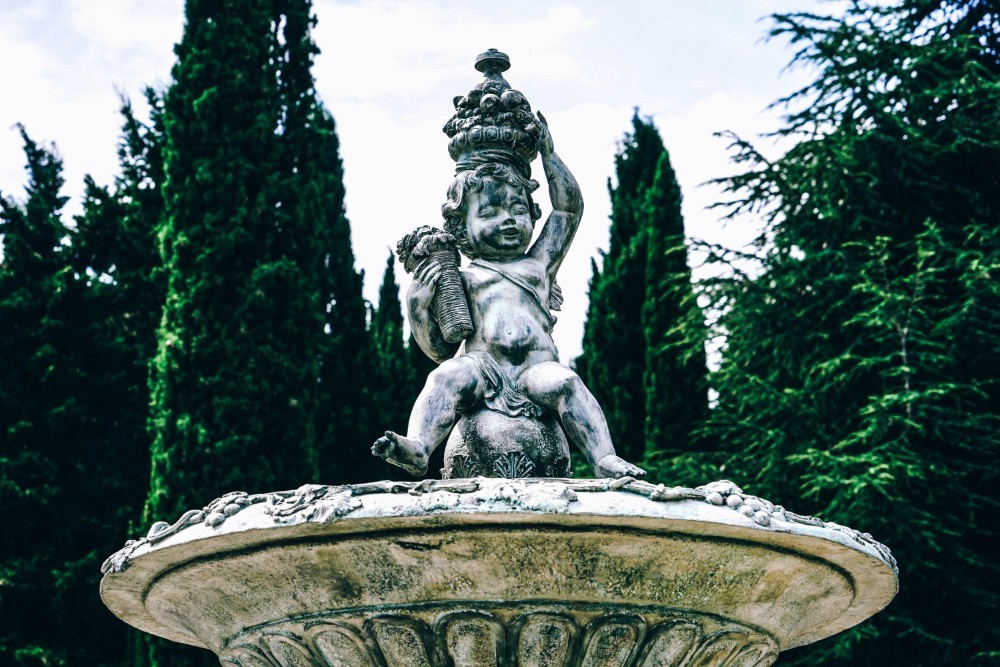 White Statue Fountain Photographed in front of Tall Trees