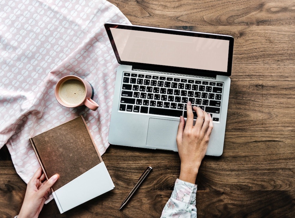 person using silver MacBook on top of brown table