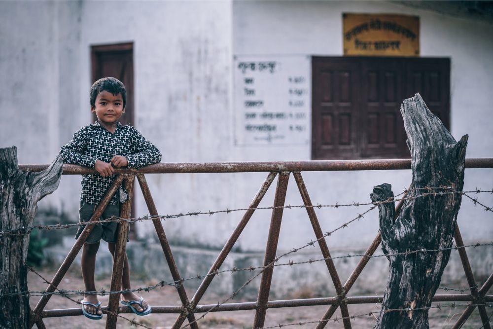Cute Nepali Boy Standing at a Fence and Looking at the Camera