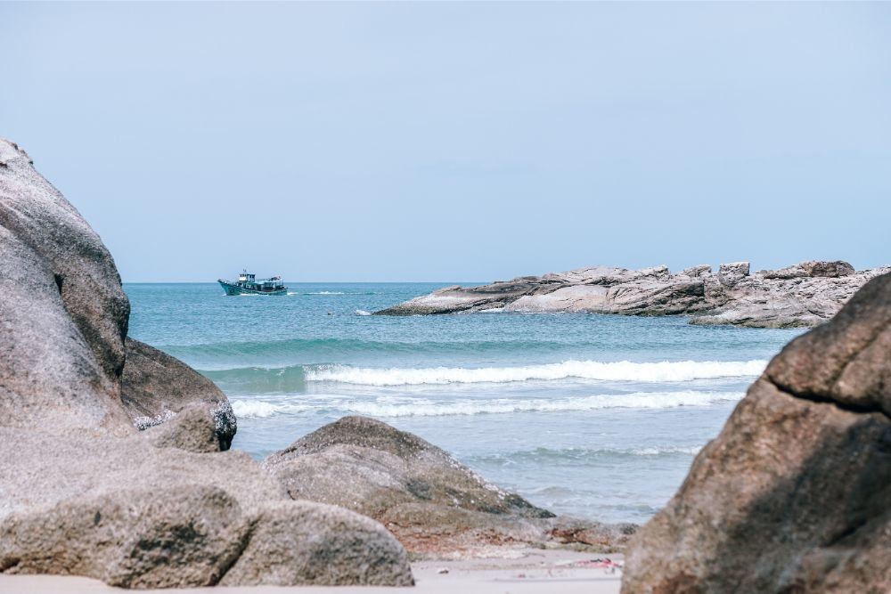 Fishing Boat Photographed from the Beach Behind Rocks