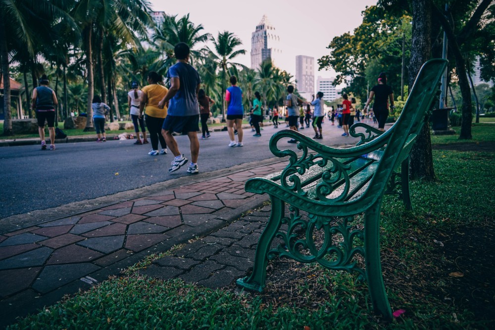 Green Metal Park Bench with People Exercising in the Background