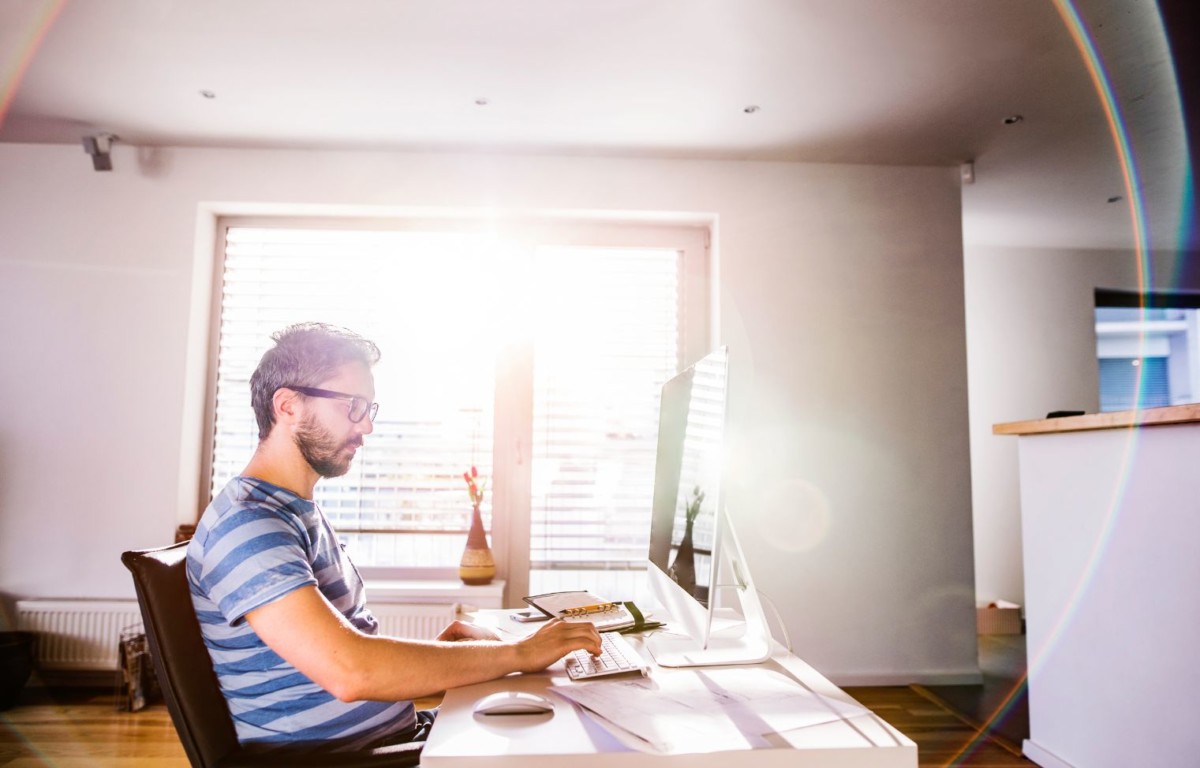 man sitting at desk working from home on computer PYAXPY