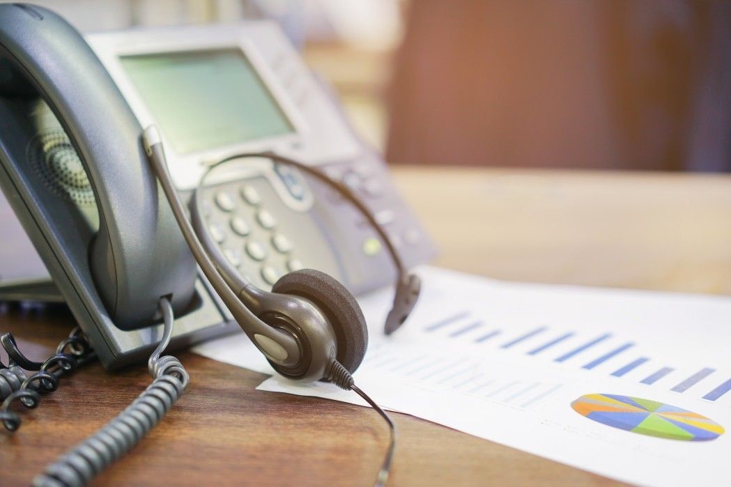 close up call center headset laying on telephone voip machine and graph stock statistics paper at t OpePBG