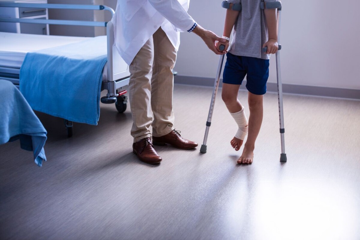 doctor assisting injured boy to walk with crutches RCMJW