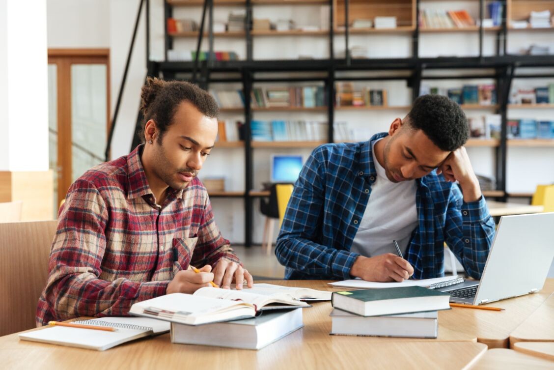 two multicultural male students studying with lapt PHMT