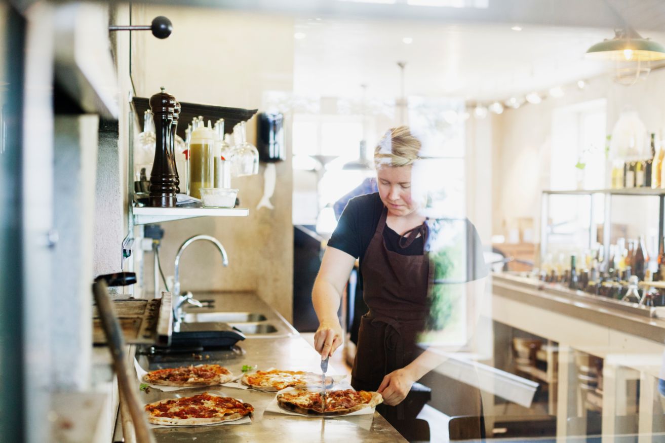 female chef cutting pizza in commercial kitchen PPDWT