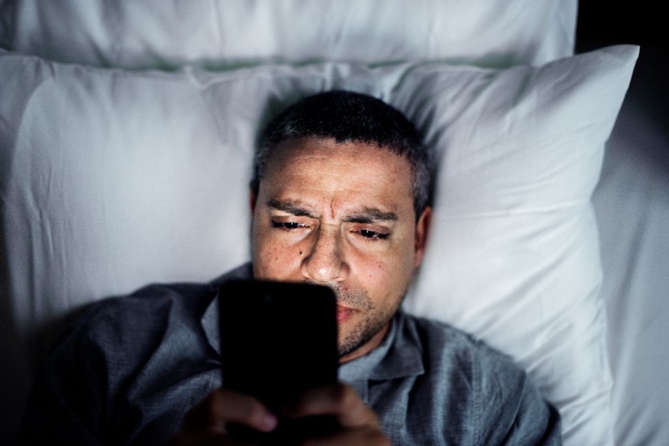 man using phone on a bed RGCJL