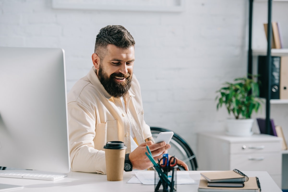 laughing businessman sitting in office and looking at smartphone