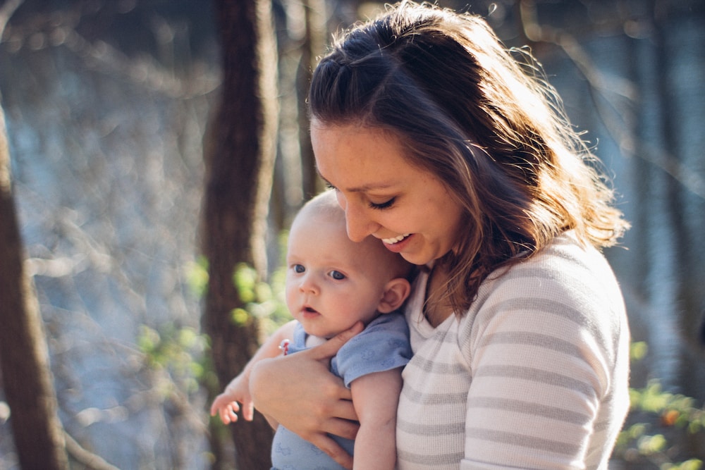 woman carrying baby near trees